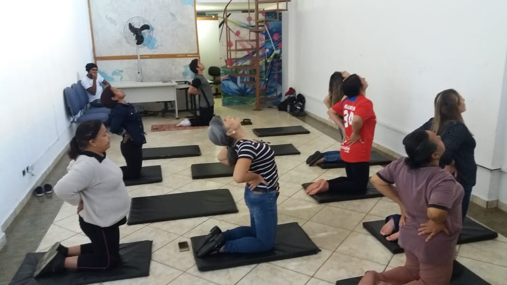 Imagem colorida, com várias pessoas realizando uma posição de yoga.